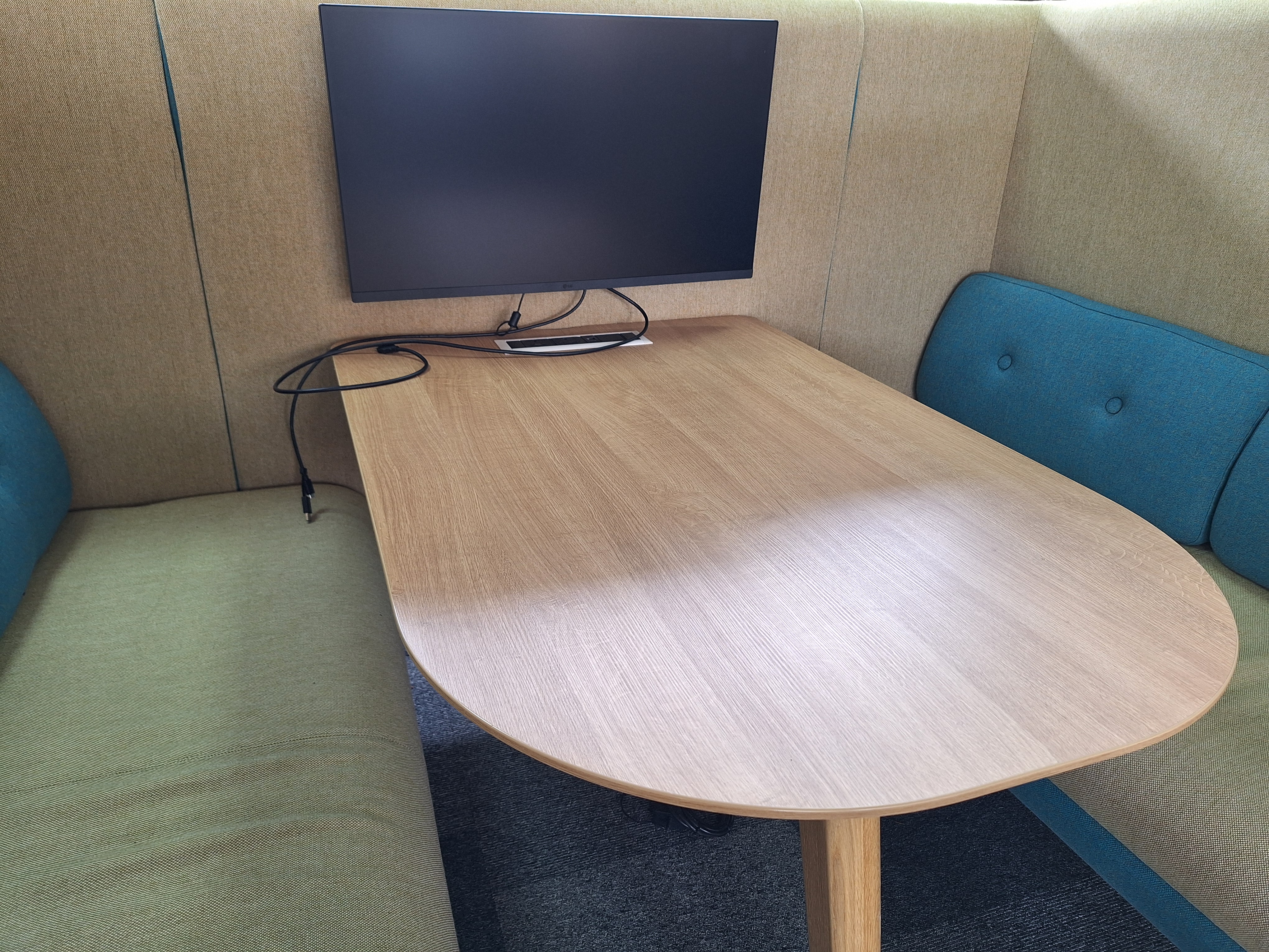 Image showing a desk a high backed seating area with a central desk and a large screen with cables to plug in laptops too.